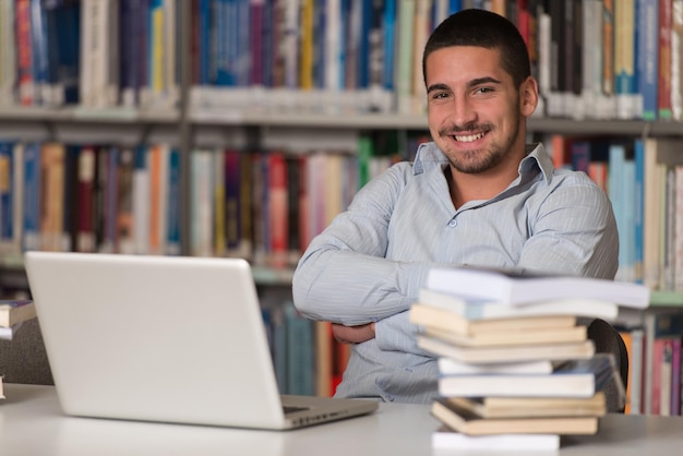 In The Library  Handsome Male Student With Laptop And Books Working In A High School  University Library  Shallow Depth Of Field