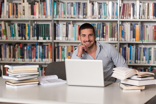 In The Library  Handsome Male Student With Laptop And Books Working In A High School  University Library  Shallow Depth Of Field