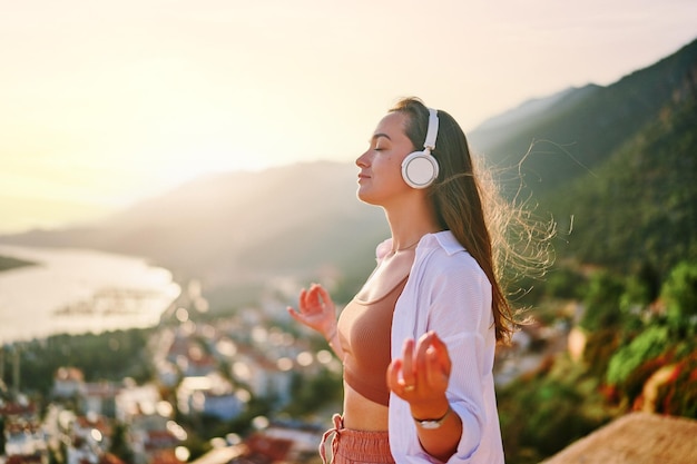 inspired spiritual female meditate alone with hands at lotus pose and closed eyes while listening calm music at sunset relief stress and healthy minds
