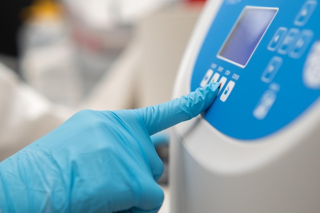 Laboratuvar çalışanı elinin kauçuk eldivenlerle numune hazırlama için santrifüjde parametreleri ayarlaması yakın çekim