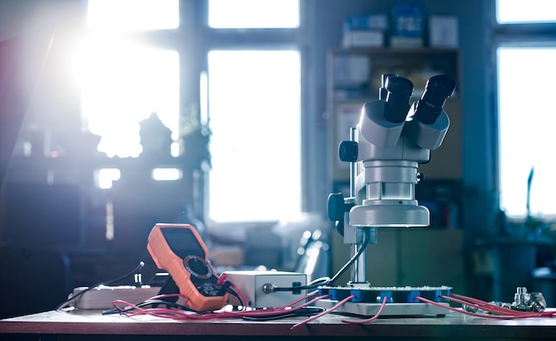Large modern electron microscope. Microwave coaxial connector and electronic digital multimeter on workshop table. Research of high-frequency radio electronic components in a scientific laboratory