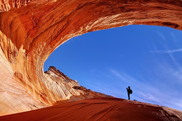 Fotoğraf low angle view of person standing at natural arch against blue sky
