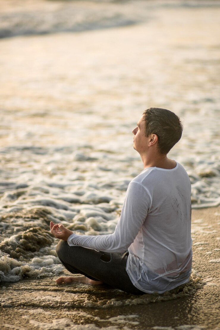 Fotoğraf man meditating at beach during sunset
