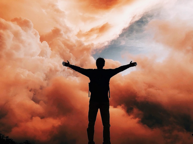 Fotoğraf man with arms outstretched standing against cloudy sky during sunset
