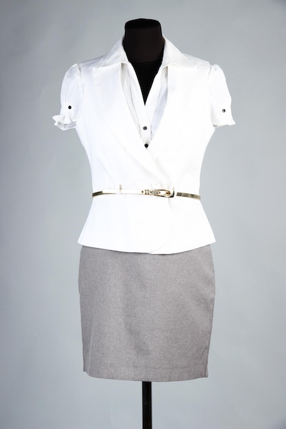 Nice blouse white jacket and gray skirt on mannequin on gray background