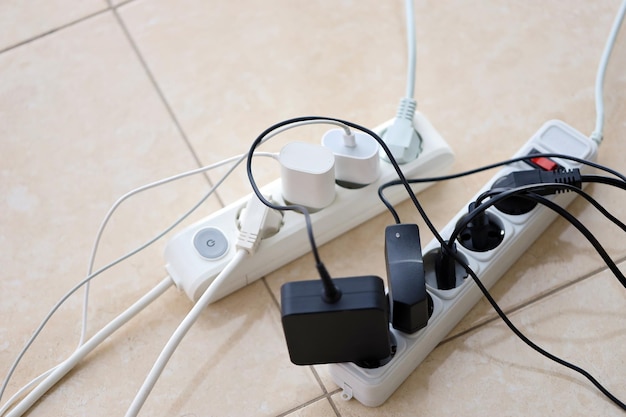 Overloaded power boards power strips with different electrical plugs on white floor
