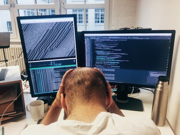 Rear view of frustrated computer programmer in front of computers in office
