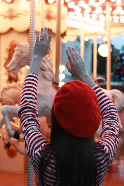 Rear view of girl standing by carousel horses at amusement park