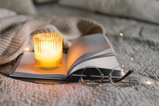 Scented candle with an open book in bed with a warm blanket