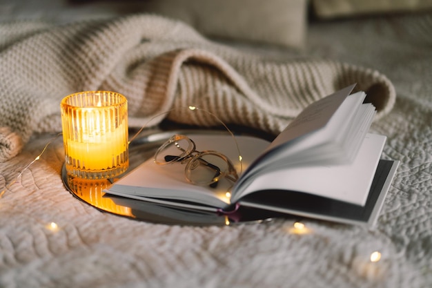 Scented candle with an open book in bed with a warm blanket