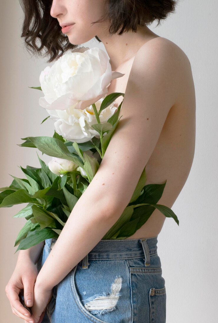 Fotoğraf side view of shirtless woman with flowers standing against wall