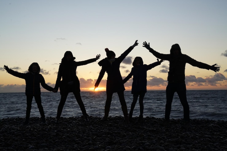 Fotoğraf silhouette people with arms outstretched standing at beach during sunset