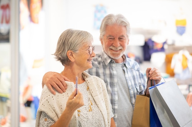 Smiling caucasian senior couple enjoying shopping man holding shopping bags the woman takes credit card in hand consumerism sales customer concept