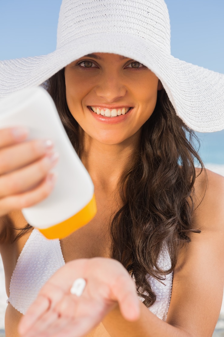 Fotoğraf smiling young brunette taking care of her body putting on sun cream