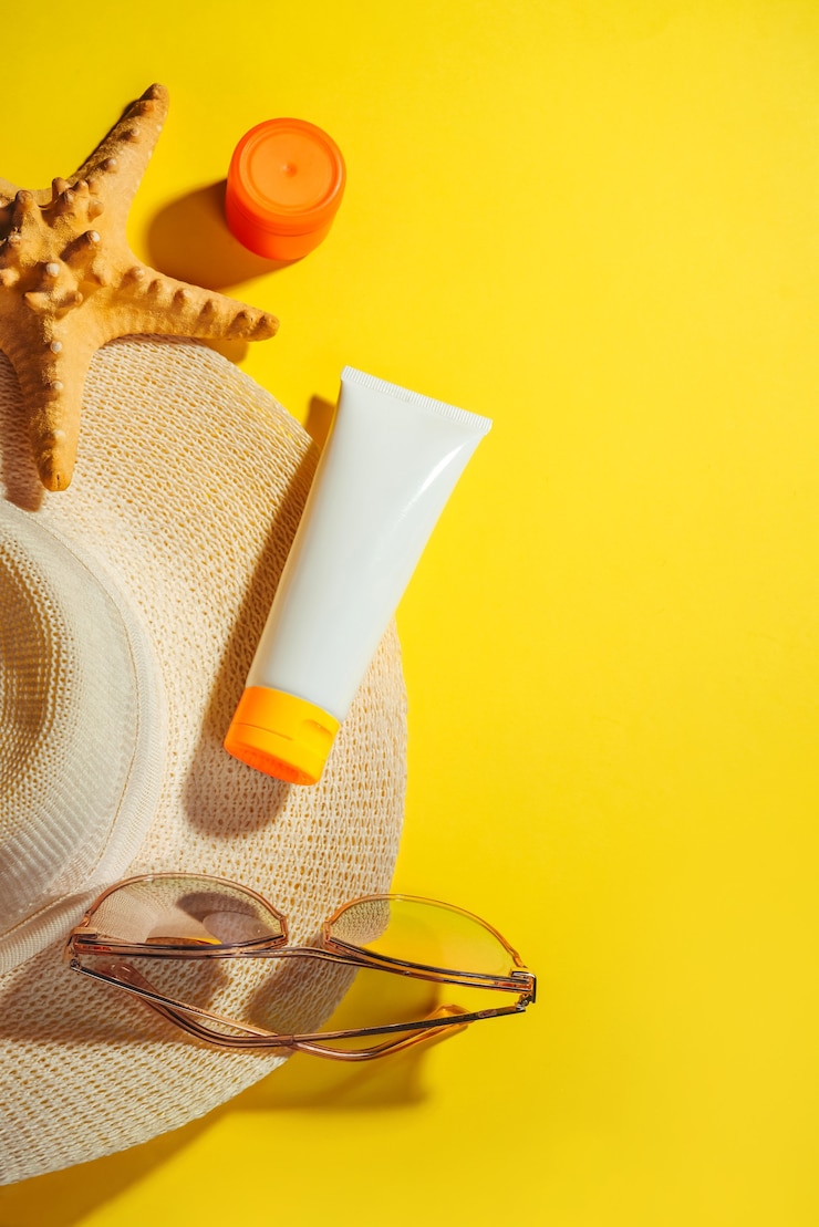 Fotoğraf sunprotection objects, sunscreen. straw woman's hat with sun glasses and protection cream spf flat lay on yellow background. beach accessories. summer travel vacation concept