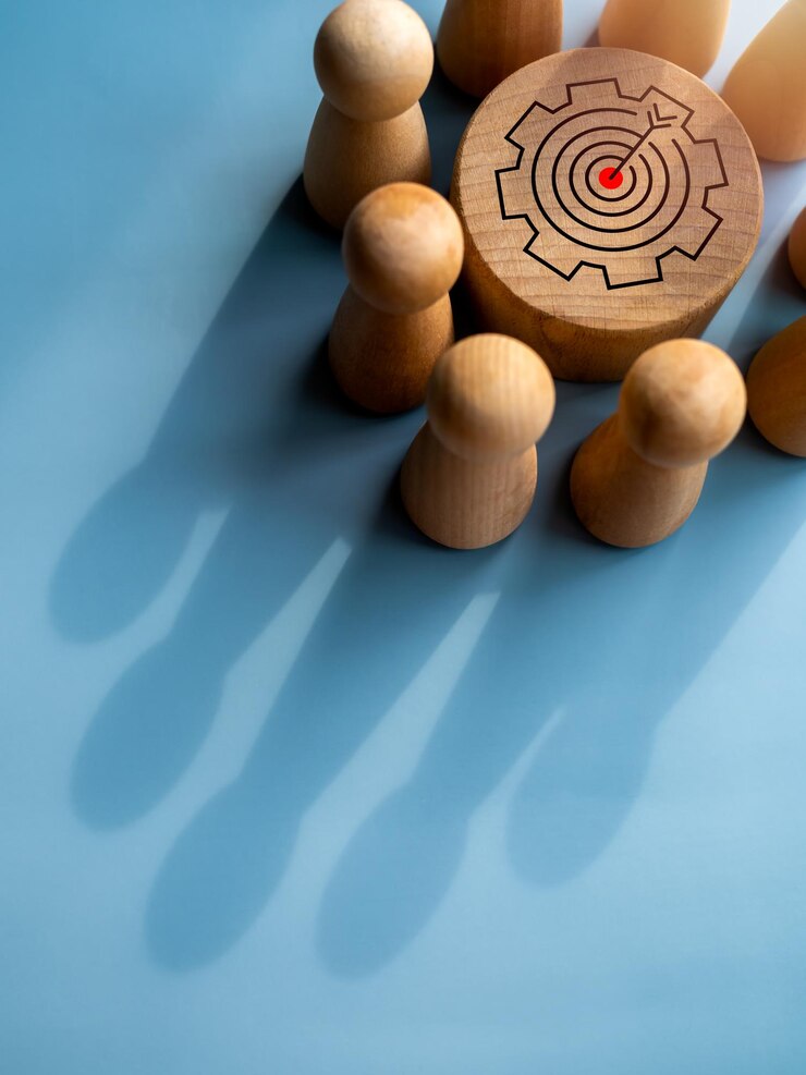 Fotoğraf target icon on round wood block surrounded with small wooden human figures made a crown shape shadow on blue background business goal and success leadership teamwork power and confidence concepts