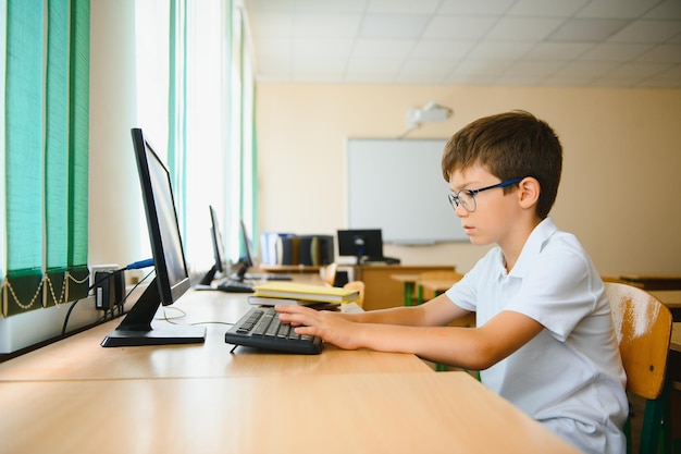 teenage boy smiling while using computer at desk in classroom
