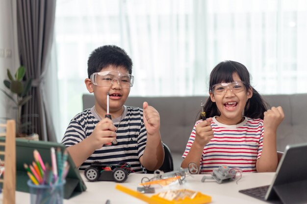 Two Asian children having fun learning coding together learning remotely at home STEM science homeschooling education fun social distancing isolation new normal concept