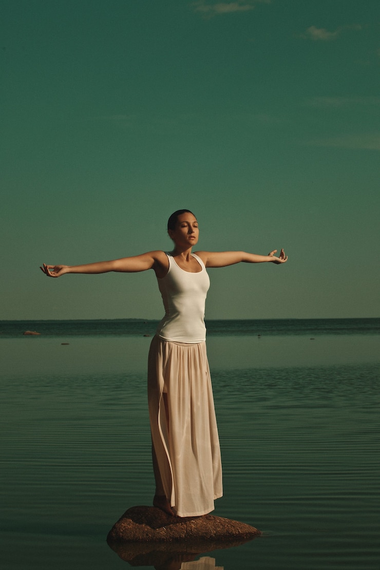 Fotoğraf woman meditating in a yoga pose on the beach at sunset
