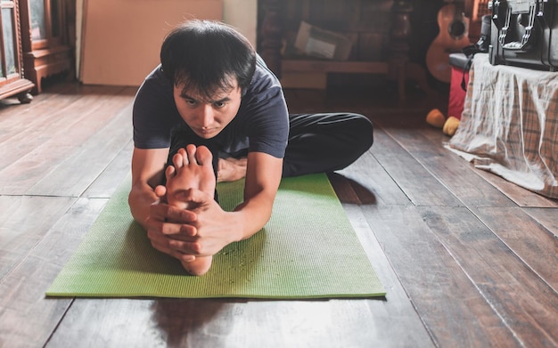 young asian man practicing yoga in a wooden room sitting in pose janu sirsasana healthy life concept