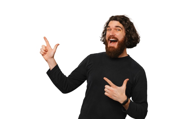 Young excited bearded man with long hair pointing aside with both hands