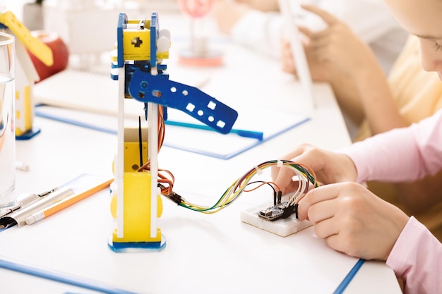 Young Girl Connecting Wires To Robotic Arm During Science Class