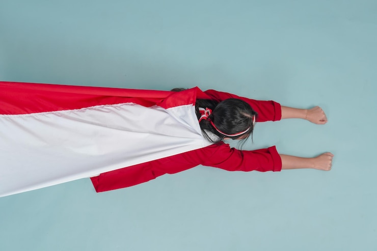 Fotoğraf young indonesian woman wearing country flag on her back and raising hands superhero flying gesture