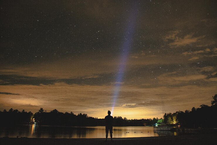 Fotoğraf young man painting with light by lake against starry sky