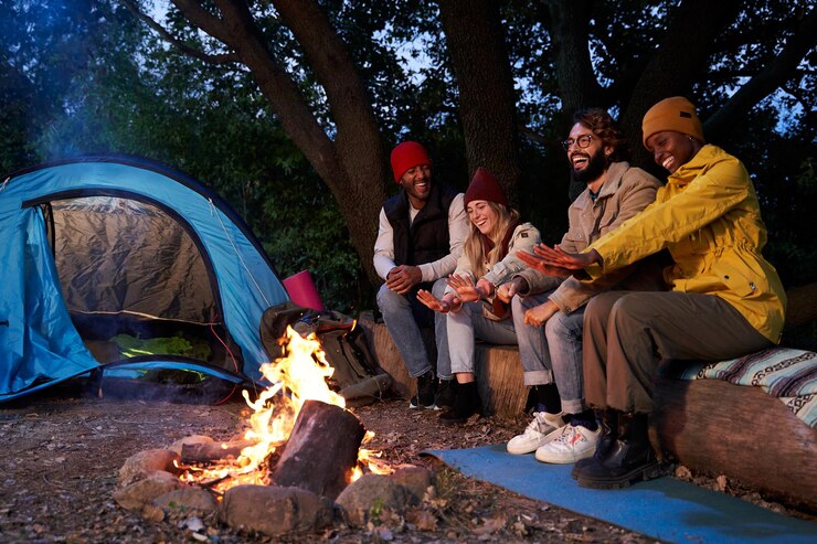 Fotoğraf young multiethnic group of friends camping outdoors sitting around campfire on the forest