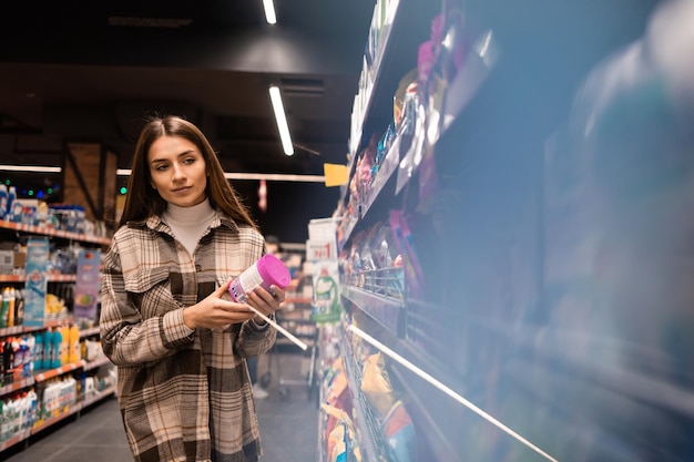 young woman chooses a cleaning product in a supermarket