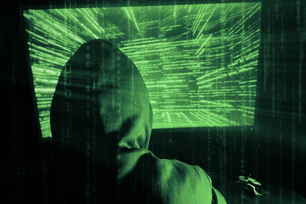 A man hacker in a hood in a dark room