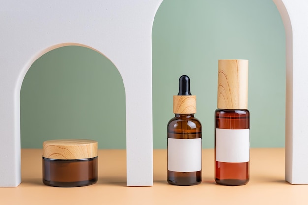 A mockup of a brown cosmetics bottles with dispenser and white label and bottle with pipette in white arched doors for cosmetics photography on beige colored background