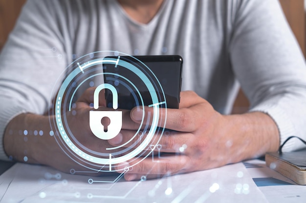A programmer is browsing the Internet in smart phone to protect a cyber security from hacker attacks and save clients confidential data Padlock Hologram icons over the typing hands