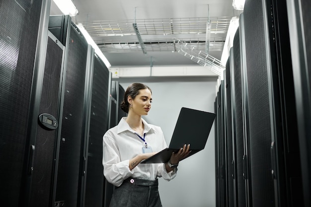 A woman in a white shirt diligently works with a laptop in a hightech server room