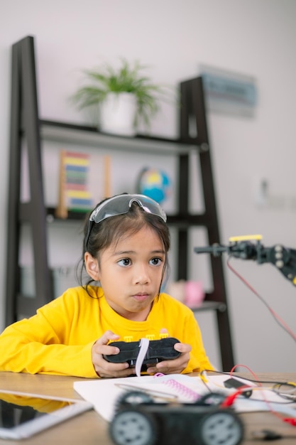 A young girl in a yellow shirt is playing with a remote control car