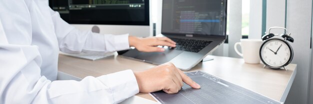 Aasialainen nainen ohjelmoija kirjoittaa lähdekoodeja ohjelmointia tietokoneella toimistossa, freelancer-verkkokehittäjäkonsepti.