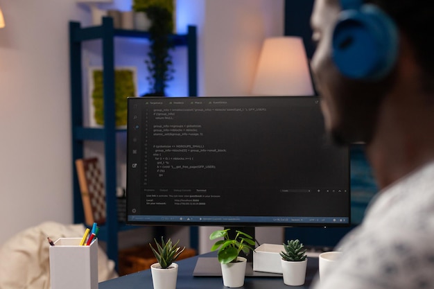 African american young developer programming software for website typing html code developing application. Businessman wearing headphones working at infographics javascript. Remote work from home