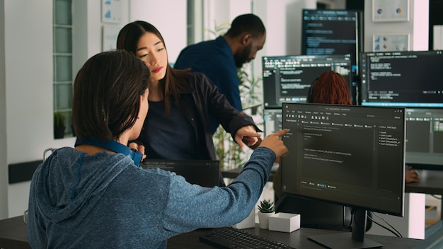 Asian database developers analyzing compiling code on multiple screens, working on new app interface development. System engineers using terminal window with firewall server data.