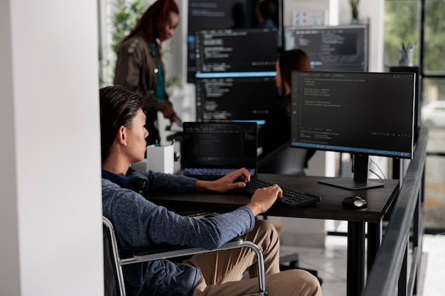 Asian disabled software developerr typing programming language on computer, using big data and firewall server. System engineer with physical impairment in disability friendly it agency.