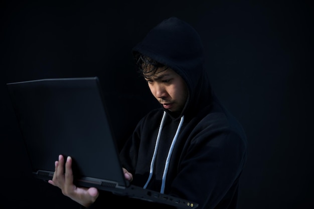 Asian hacker in black hood on black backgroundHack passwordhacking safety systems to steal information
