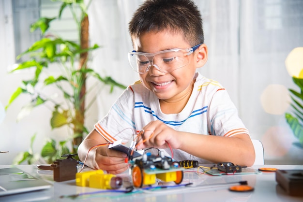 asian kid boy plugging energy and signal cable to sensor chip with arduino robot car