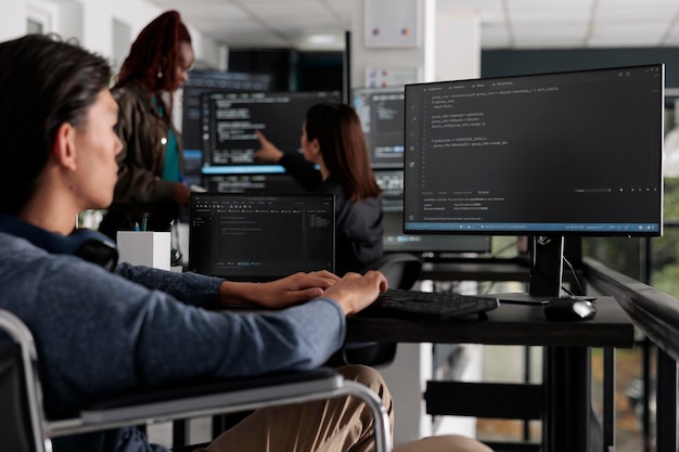 Asian programmer with physical disability typing html code on computer, working with cloud computing terminal window. Web developer in wheelchair writing ai algorithm in it software company.