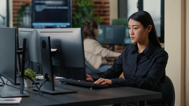 Asian software developer focused on writing code encounters unexpected compiling error sitting at desk in cyber security development office. Programer having system failure while creating algorithm.