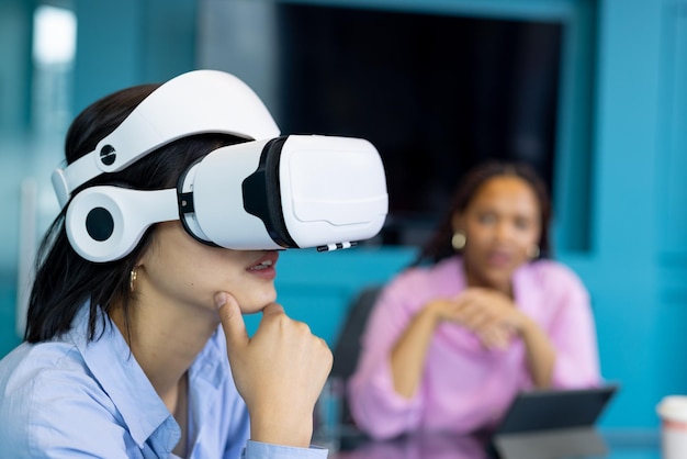 Asian young woman uses VR headset as biracial young woman observes collaborating on business