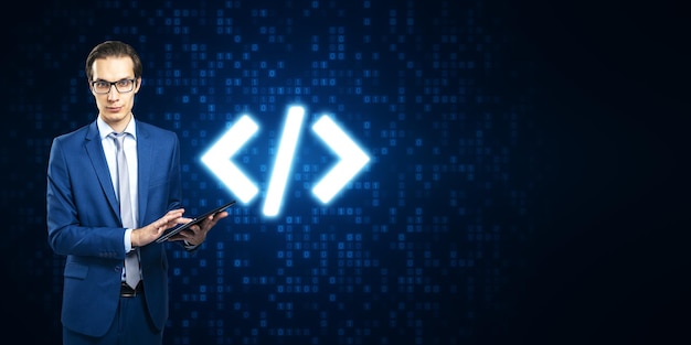 Attractive young european businessman using tablet with glowing programming code on blue binary coding background with mock up place Program and software development concept