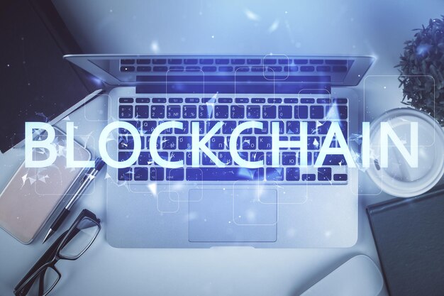 Blockchain-teemaiset hologrammi piirrokset tietokoneen yllä työpöydän taustalla. Yläkulma. Kaksi valotusta.