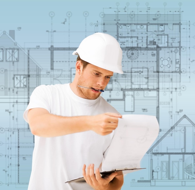 building, developing, construction and architecture concept - male architect in helmet looking at blueprint