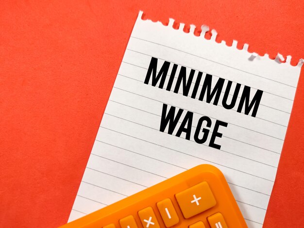 Business conceptText MINIMUM WAGE writing on notepaper with calculator on red background