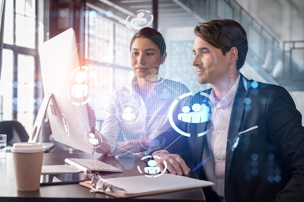 Businessman and businesswoman in formal wear working together looking for new employees to hire for international business consulting HR social media icons over modern panoramic office background