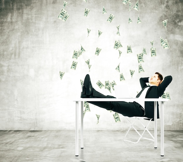 businessman on a chair in loft room with money falling from the ceiling
